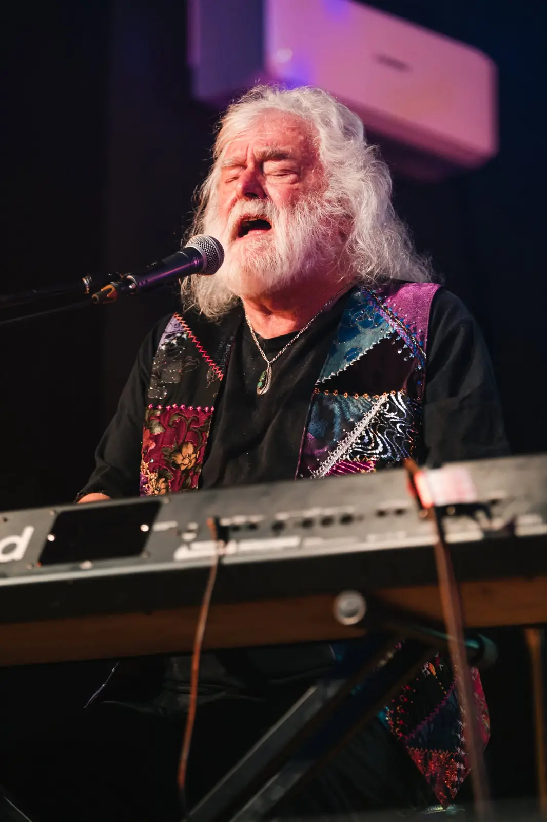 Brian Cadd singing at the keys in a patchwork jacket