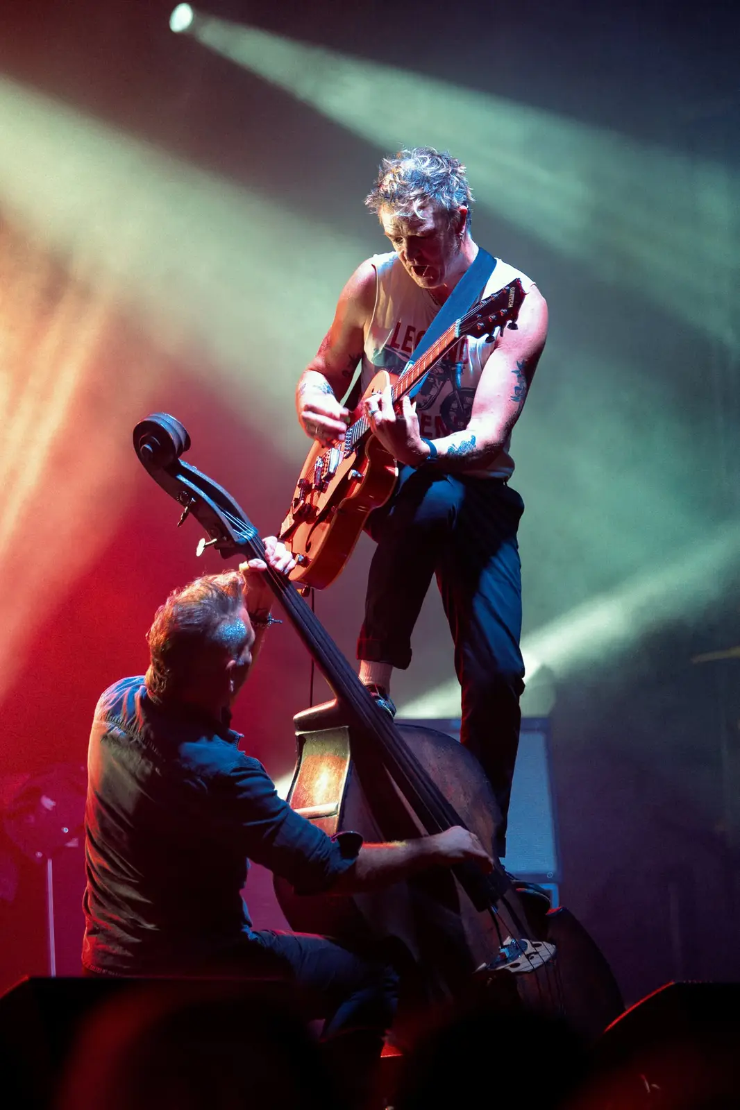 Two Living End members stacked on the double bass under teal light