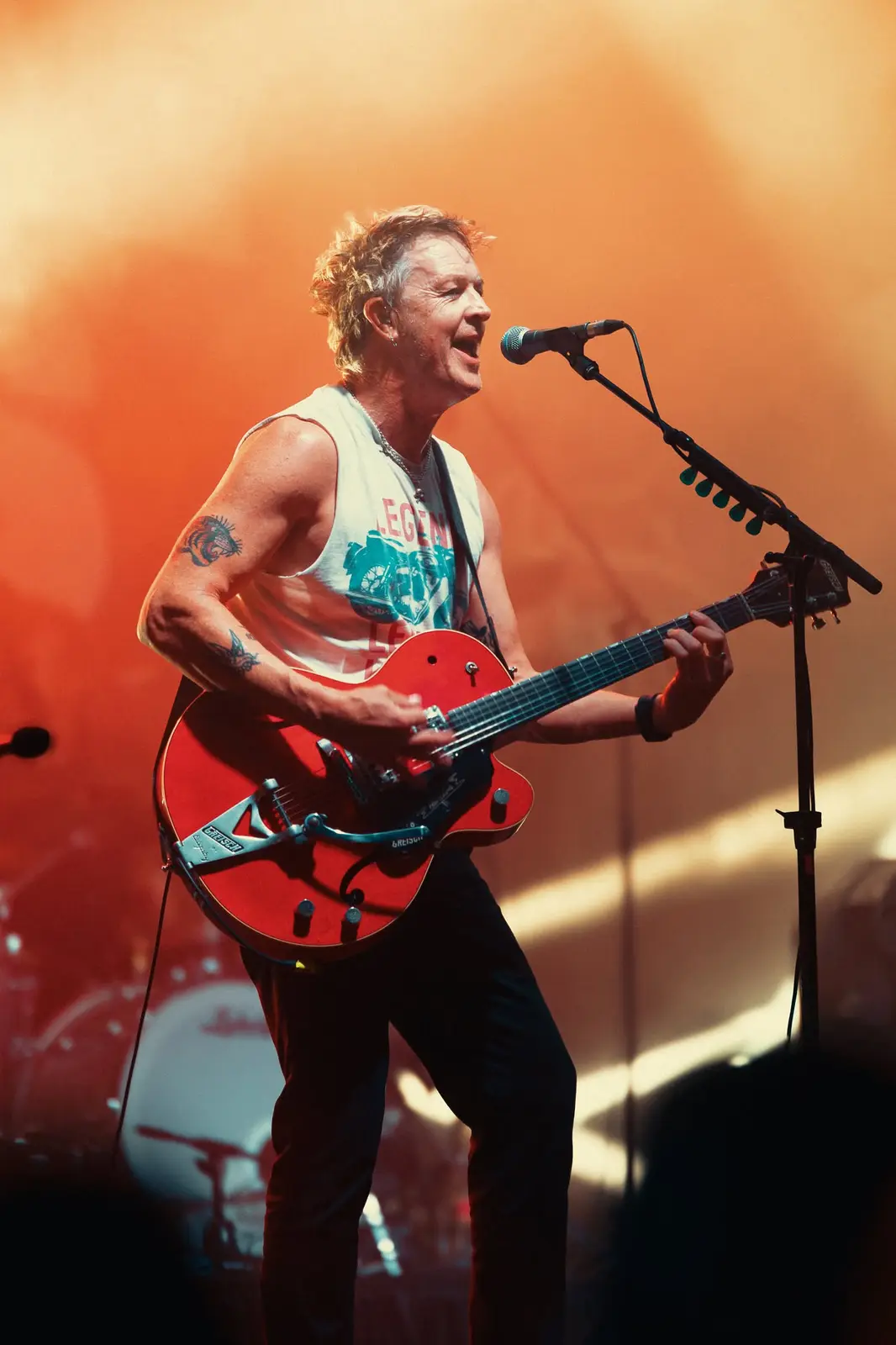Guitarist in a singlet playing a red Gretsch under orange light