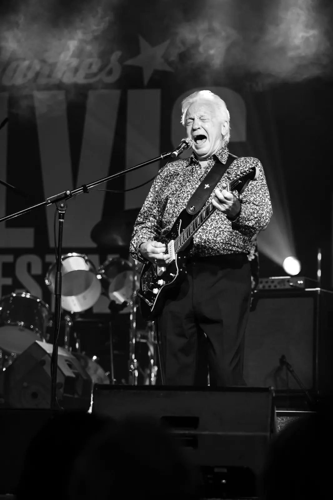 Normie Rowe singing with guitar under red light