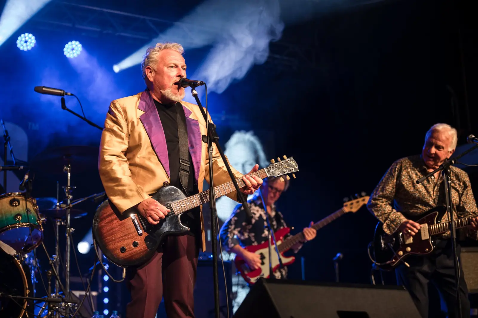 Ross Wilson in a gold jacket with guitarist in stage smoke