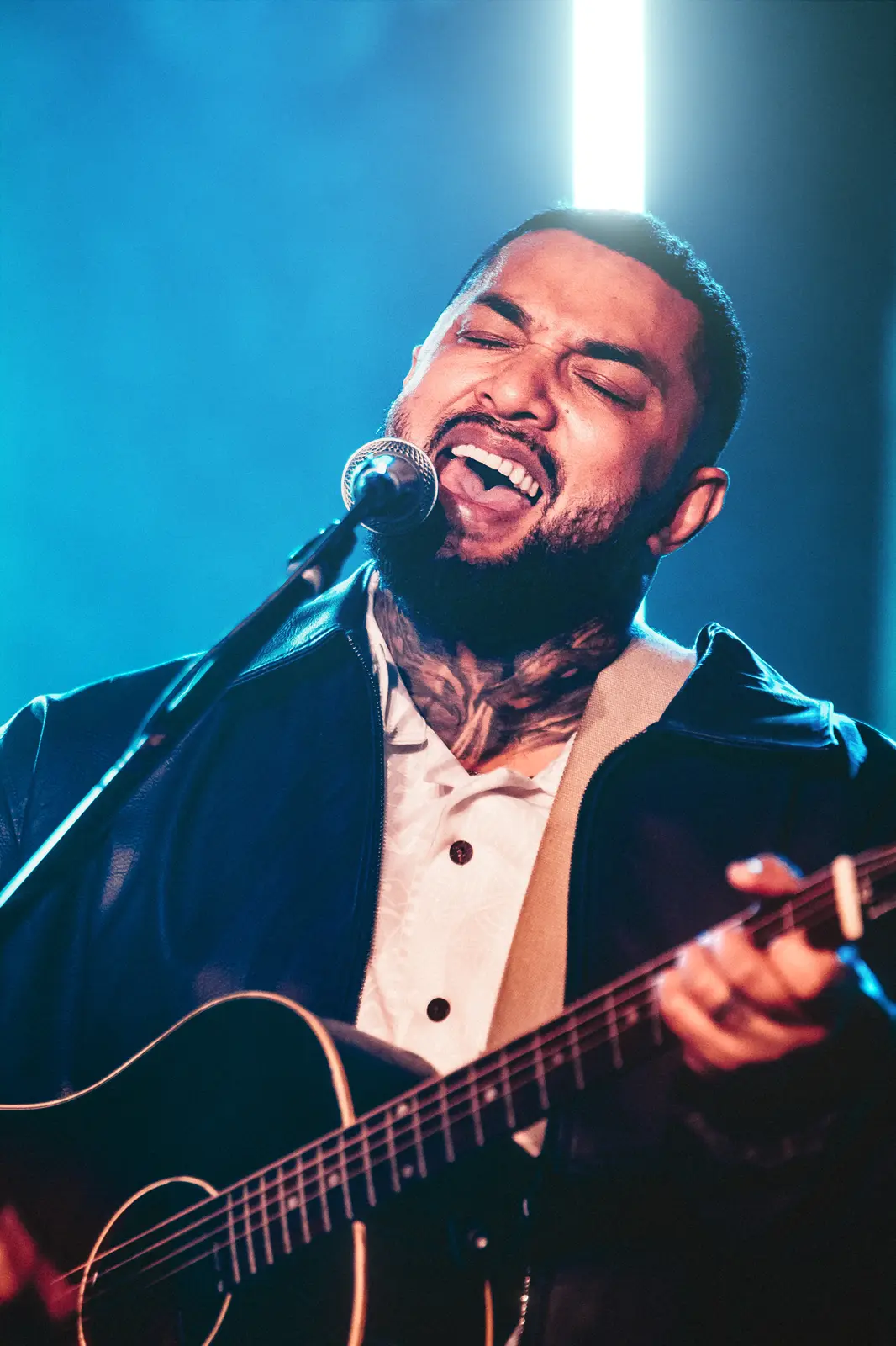 Thirsty Merc vocalist singing with guitar under blue stage light