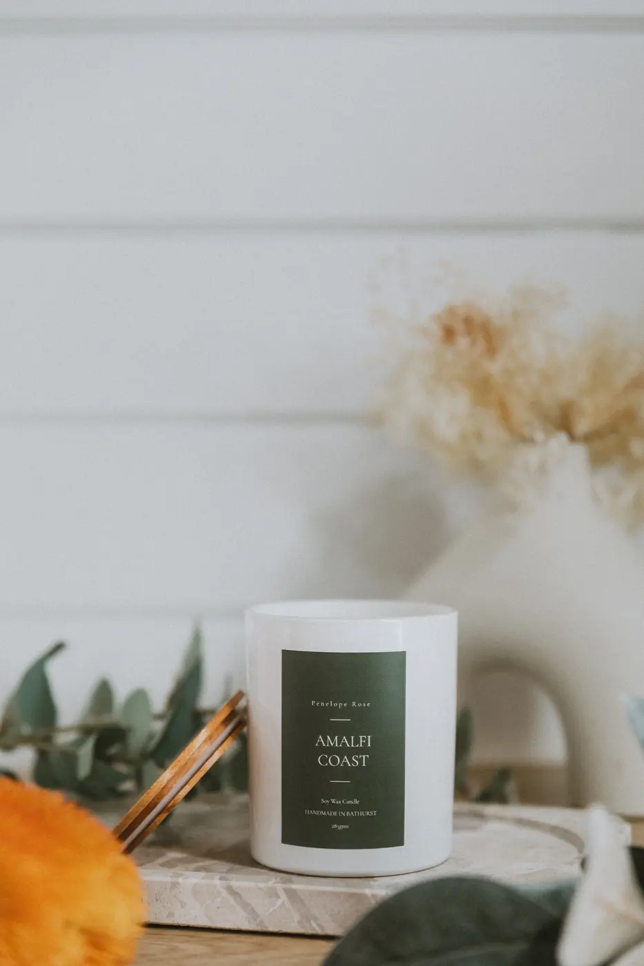 White soy candle with a green label on marble with cinnamon and eucalyptus