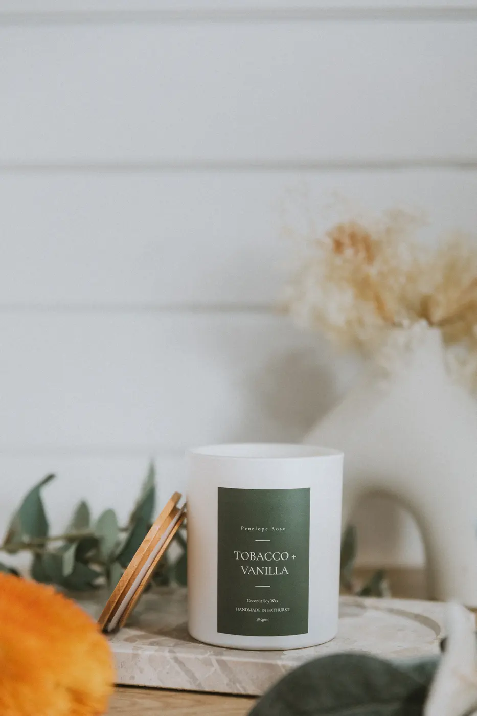 White soy candle with a dark green label, dried botanicals behind